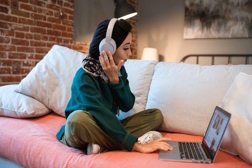 Free A woman wearing headphones sits on a couch focused on her laptop screen while working remotely. Stock Photo
