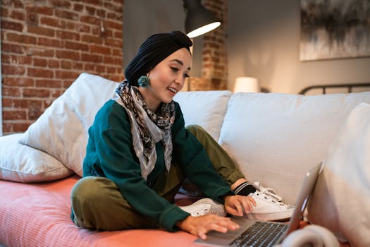 Young woman working remotely at home, sitting comfortably on a couch with a laptop.