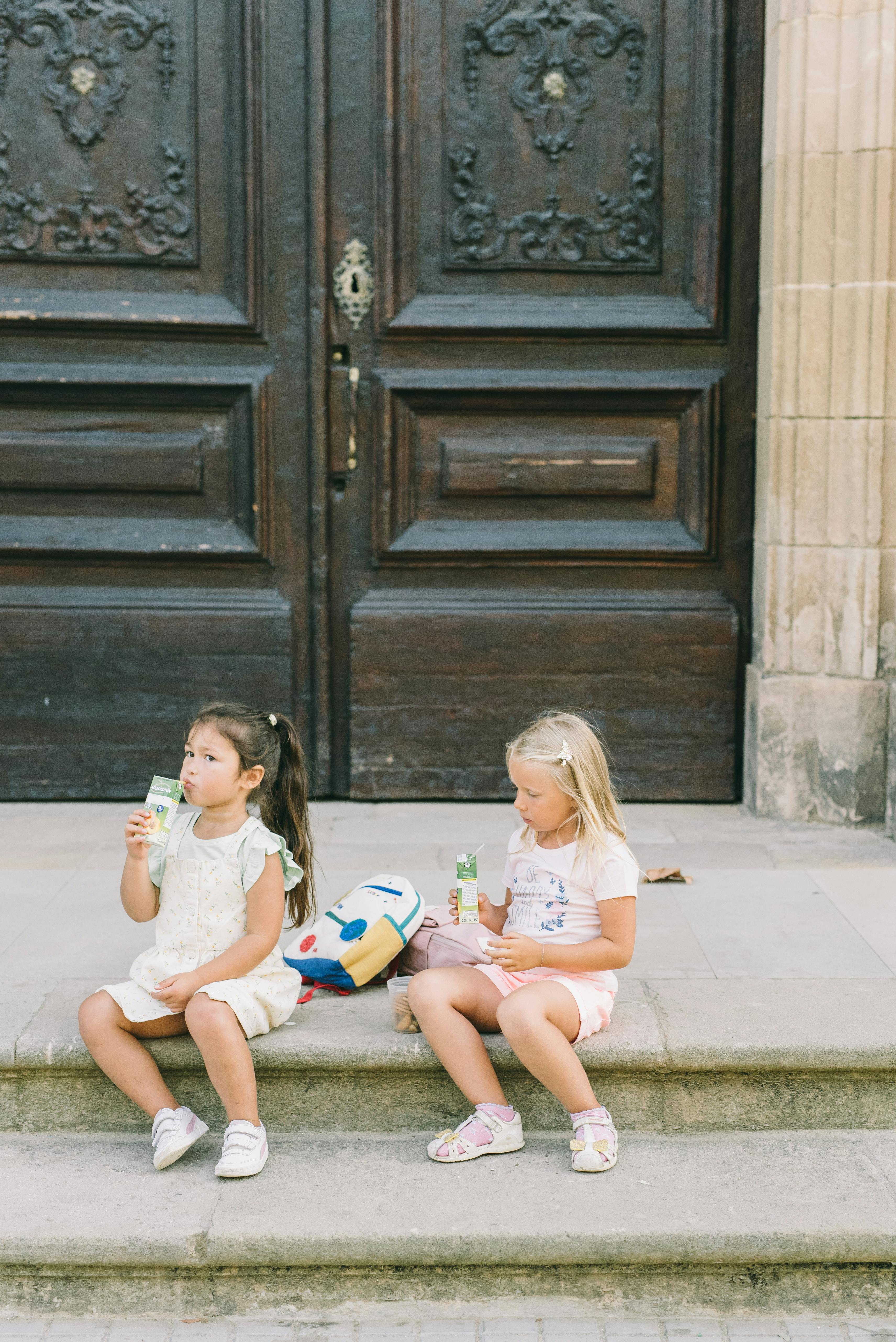 girls drinking from a juice box while sitting on stairs