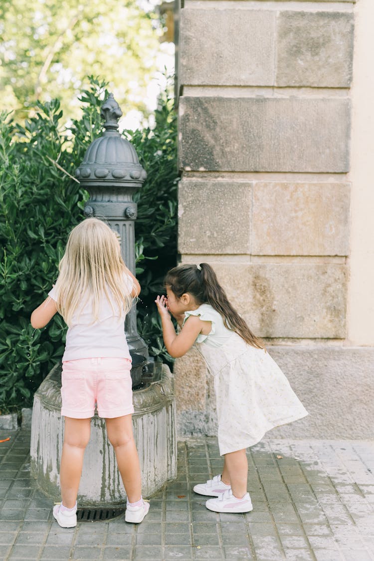 Two Girls Drinking From A Drinking Fountain