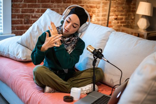 Woman podcasting at home, wearing headphones and using a microphone, creating content.