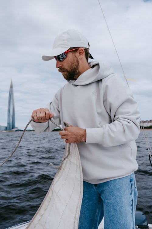 Man in Gray Hoodie and Blue Denim Jeans Holding Fishing Rod Standing on Boat