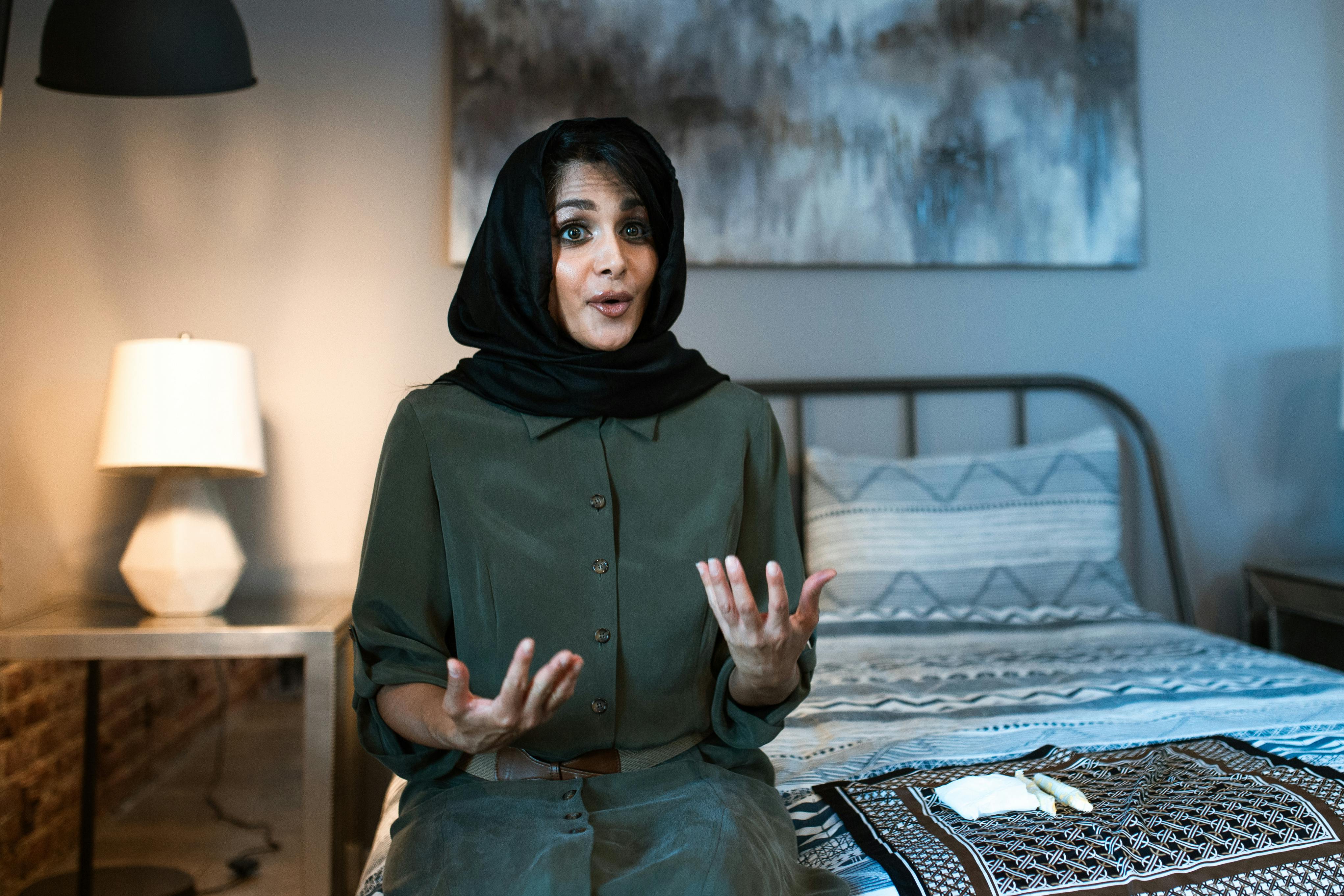 woman in green hijab sitting on bed and talking