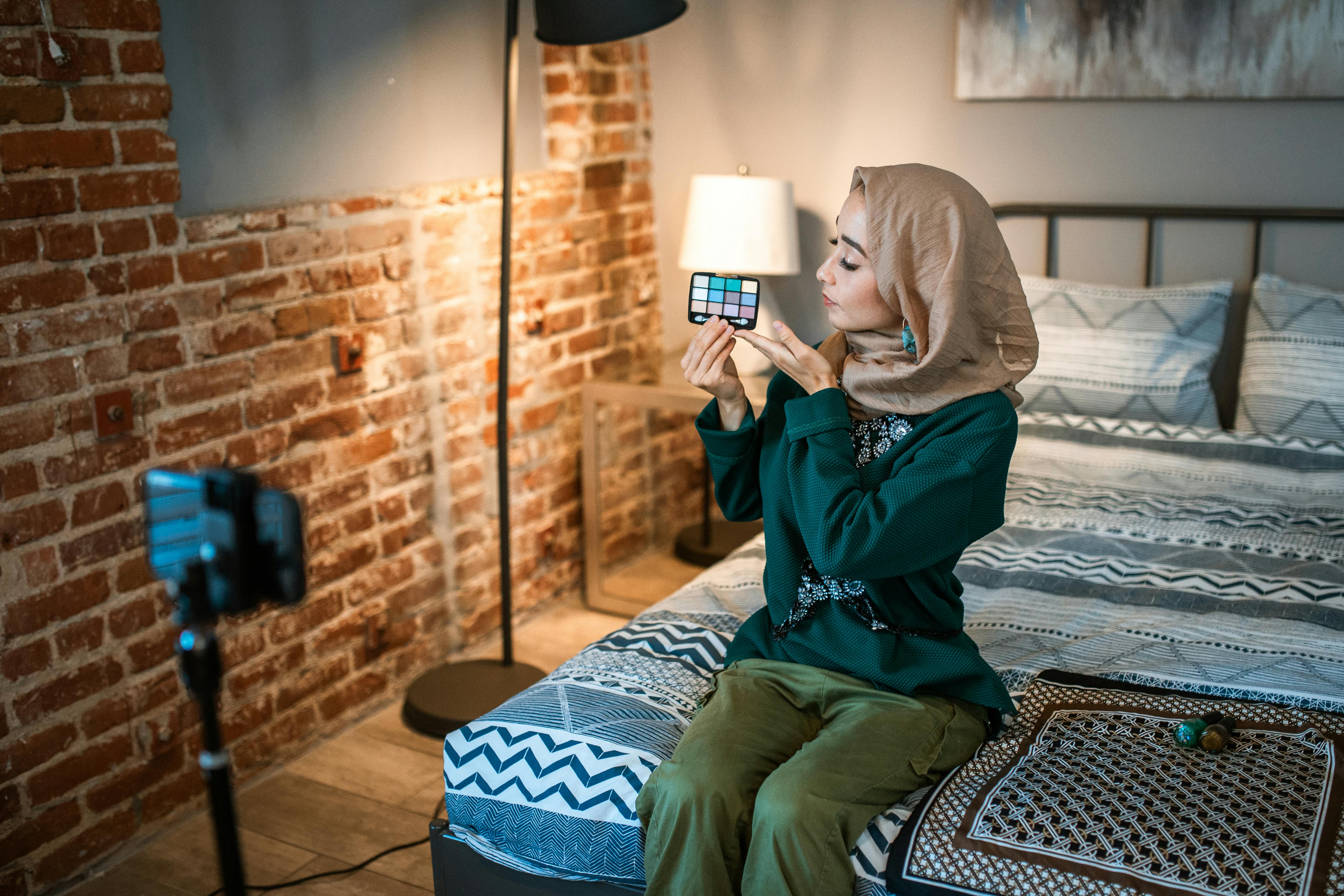 woman sitting on bed showing an eyeshadow palette