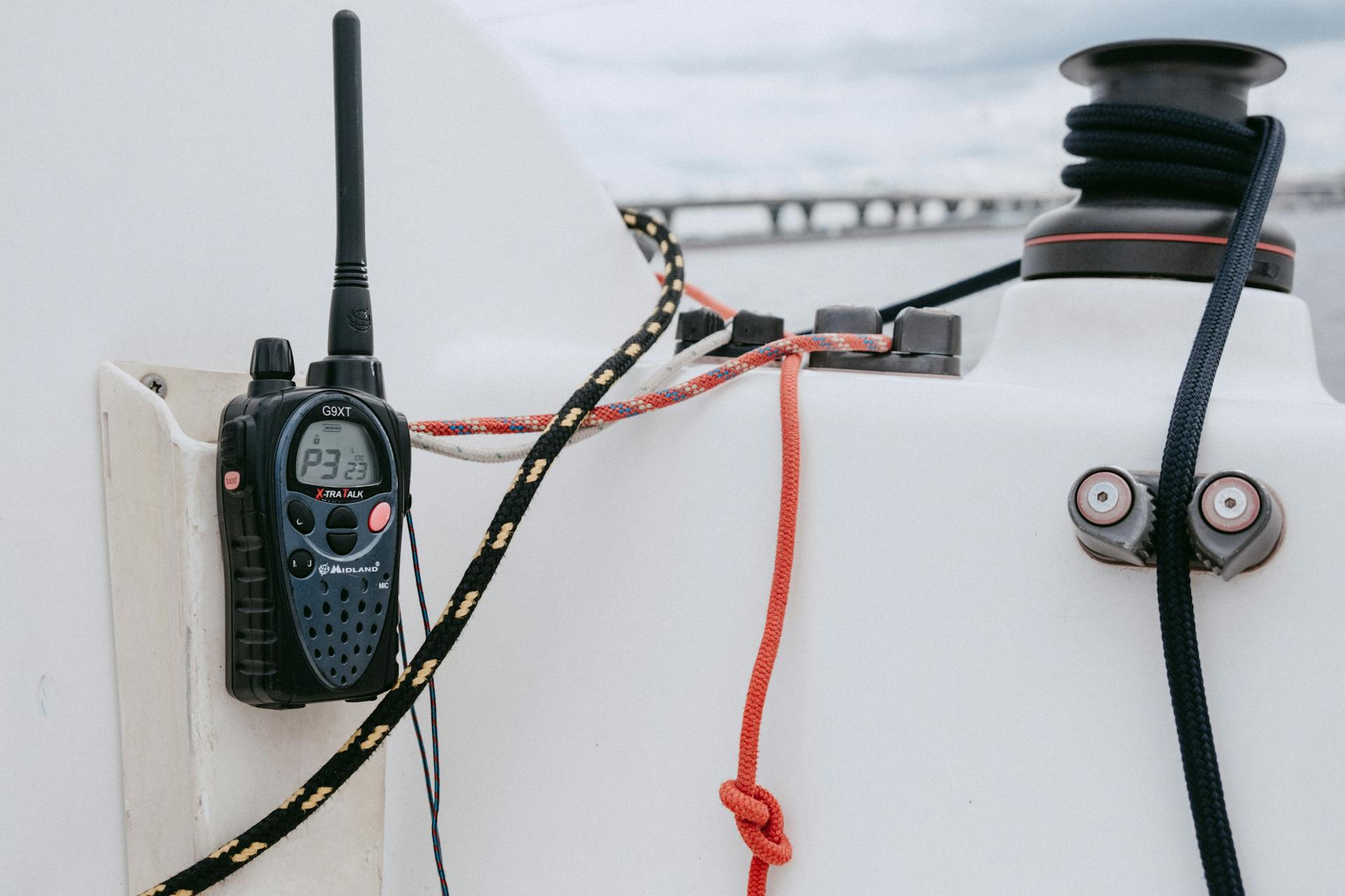 A handheld radio and nautical equipment on a yacht with ropes and a winch in focus.