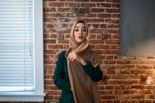 Free Portrait of a woman wearing a hijab in a modern indoor setting with exposed brick wall. Stock Photo