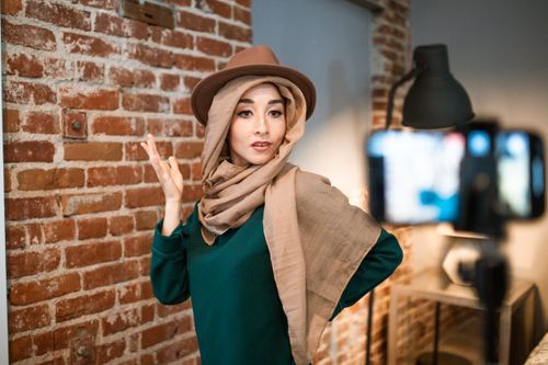 Free Stylish woman with hijab and hat posing for a vlog in a trendy indoor setting. Stock Photo