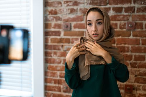 Free Stylish woman adjusts hijab during vlog against a rustic brick wall. Stock Photo