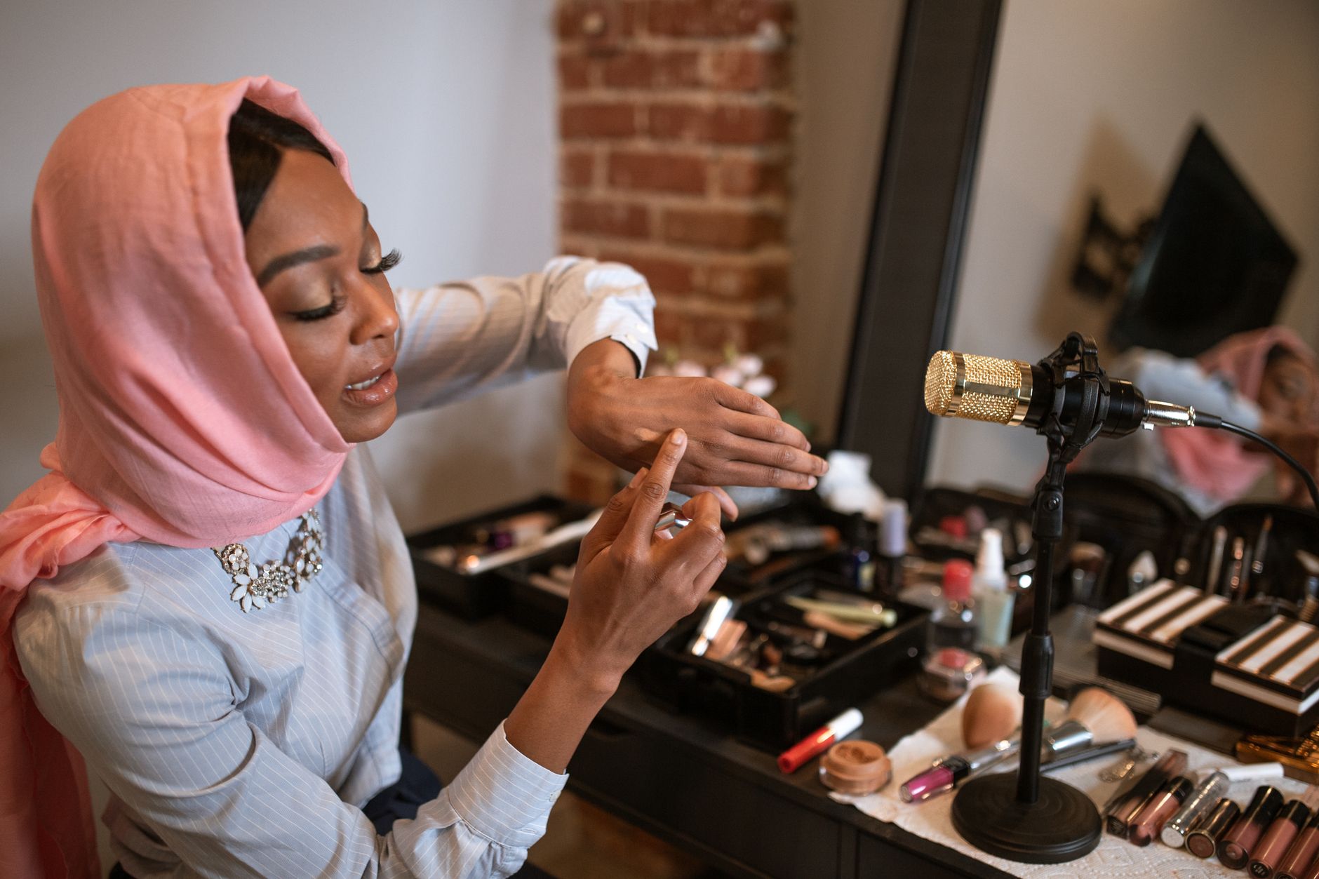 A stylish woman in a hijab demonstrates makeup products in front of a microphone for her fashion vlog.