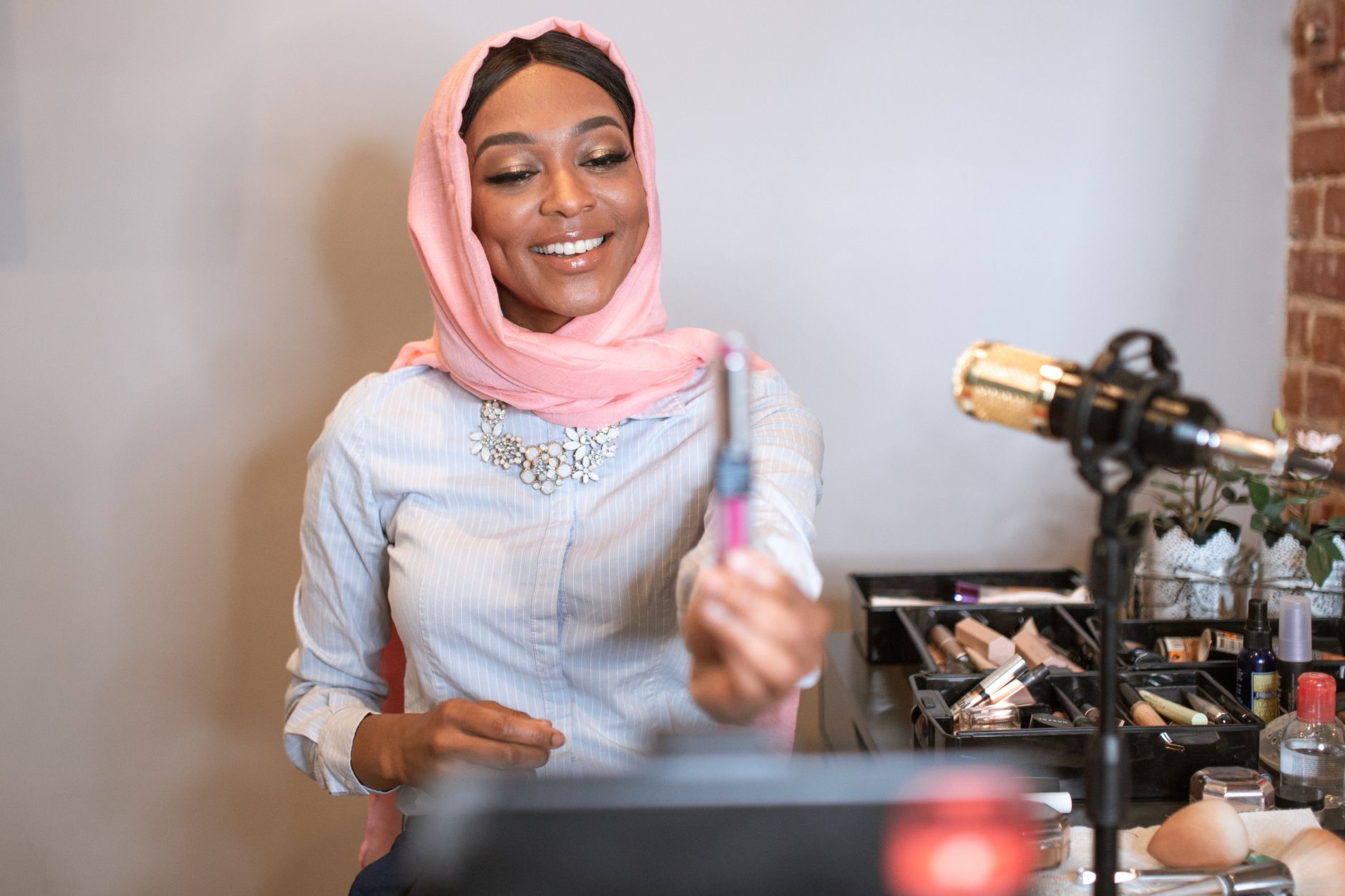 Top Skincare Hacks For Effortless Beauty 1 A smiling Muslim woman wearing a hijab records a makeup tutorial for her vlog.