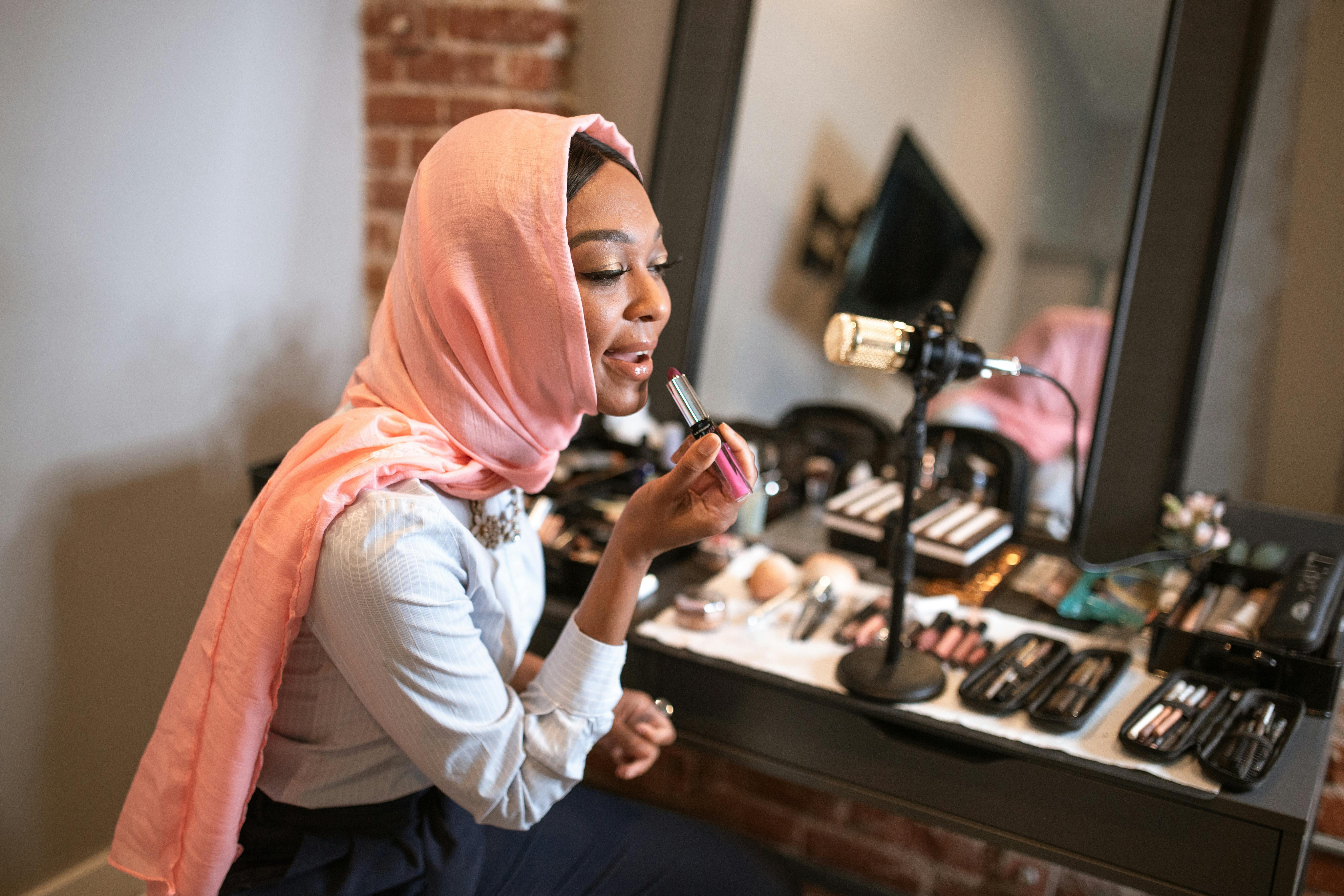 woman in pink hijab applying lipstick