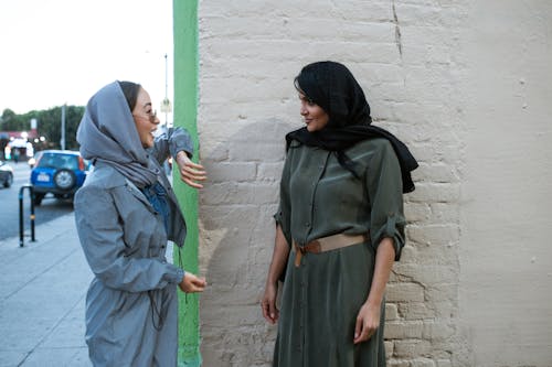 Free Women in Wearing Hijabs Chatting Near a Brick Wall Stock Photo