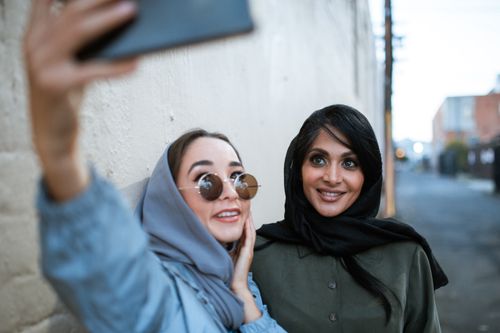 Free Two women wearing hijabs and sunglasses take a selfie outdoors. Stock Photo
