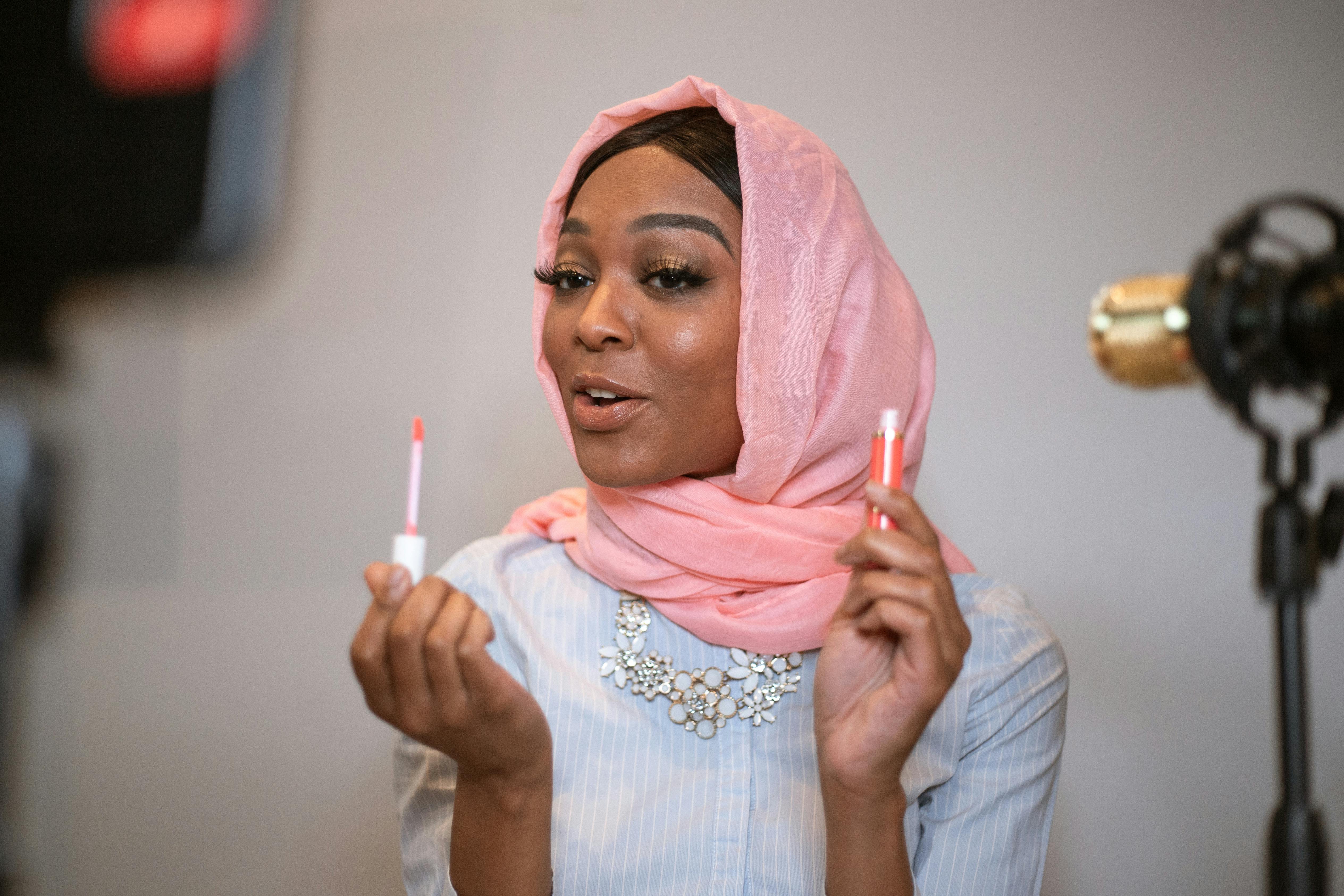 a woman wearing a pink hijab blogging a lip gloss