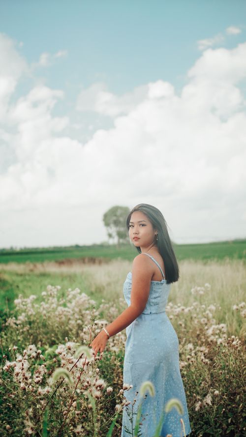 Free Portrait of a young woman in a blue dress standing in a scenic field. Stock Photo