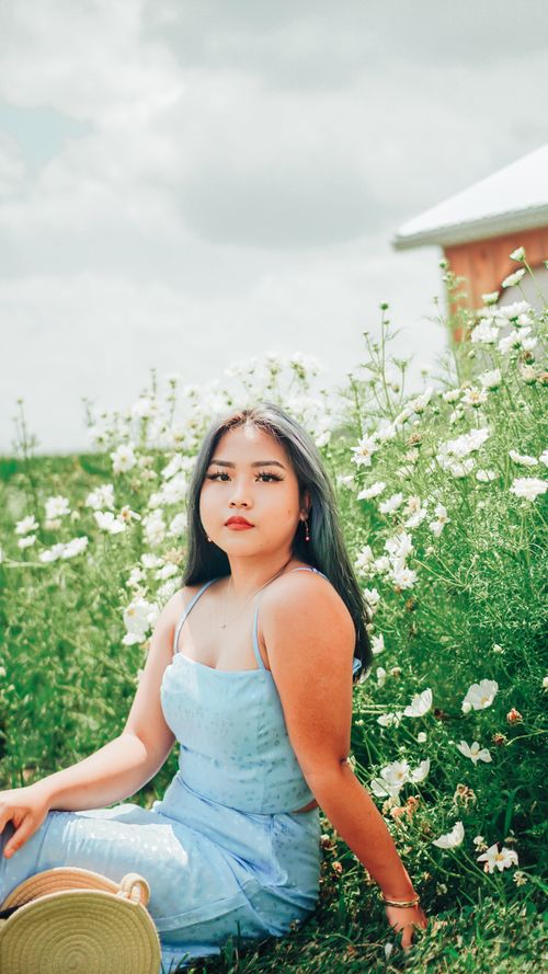 Free Serene portrait of woman in blue dress relaxing among white wildflowers on a sunny summer day. Stock Photo