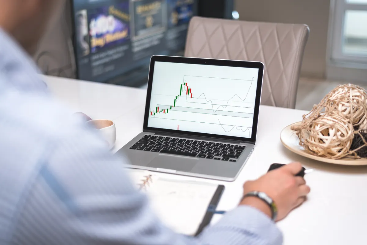 A trader reviewing live market data and analysis on a laptop in a modern office.