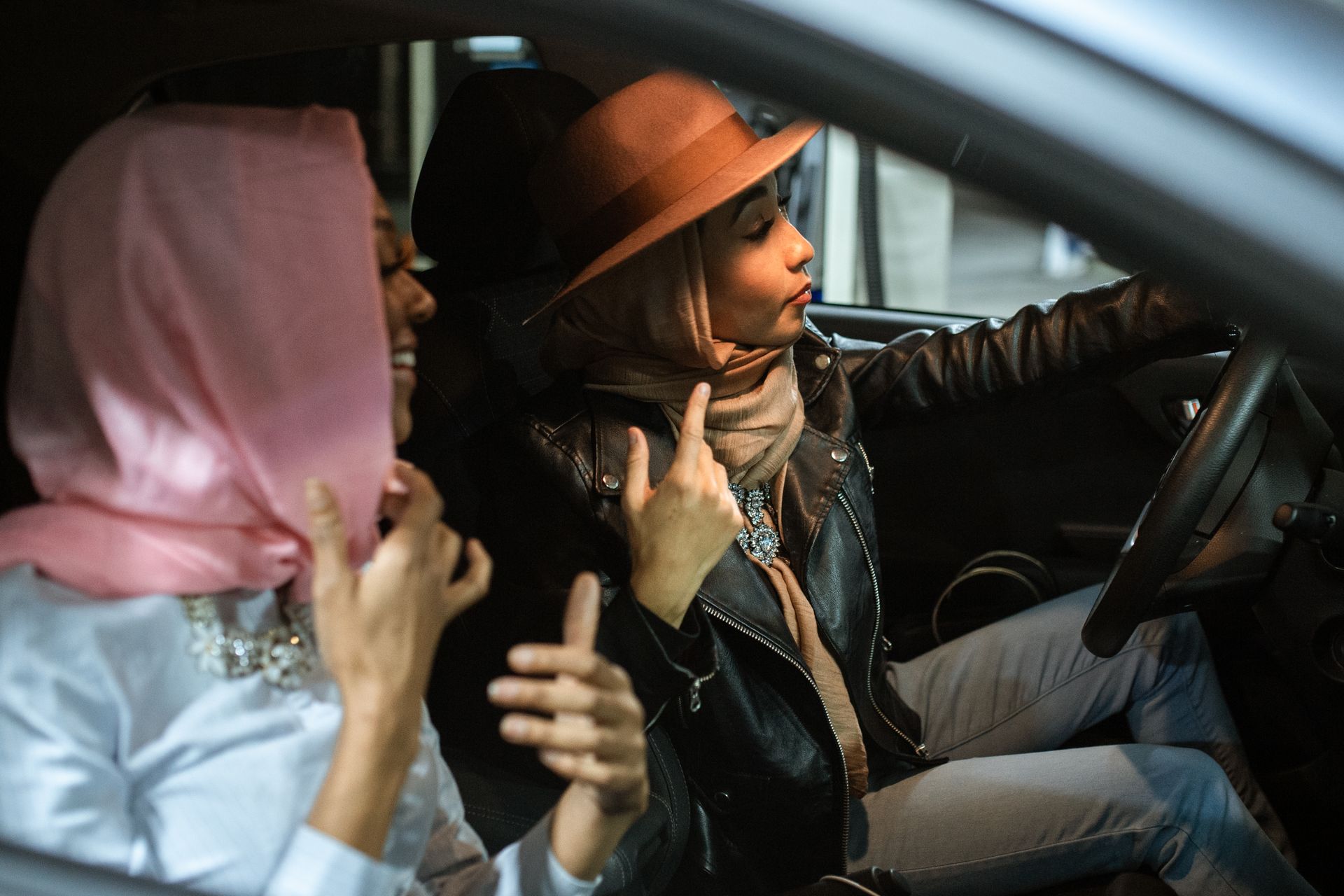 Two women in hijabs enjoy a casual drive in a car, captured from a side view.