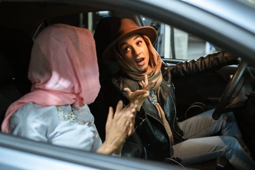 Women in headscarves have an animated conversation inside a parked car.