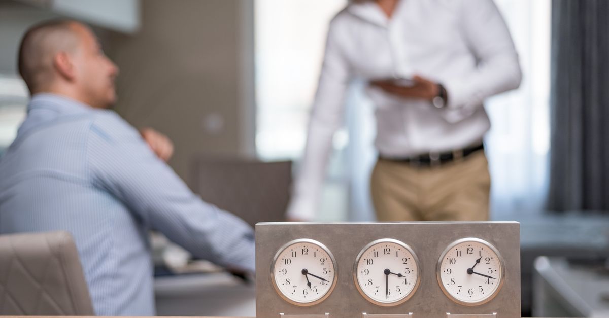 Two businessmen in an office with clocks displaying Dubai, Sofia, London time.