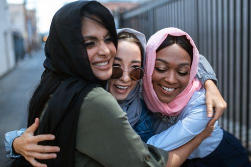 Free Three diverse women in colorful hijabs share a joyful embrace in an urban setting under daylight. Stock Photo