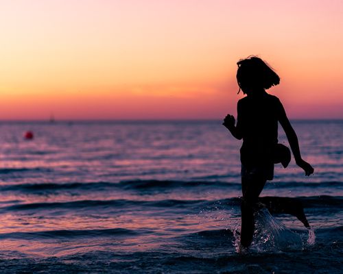 Free Side view of anonymous barefooted little girl having fun in sea at sunset during rest Stock Photo