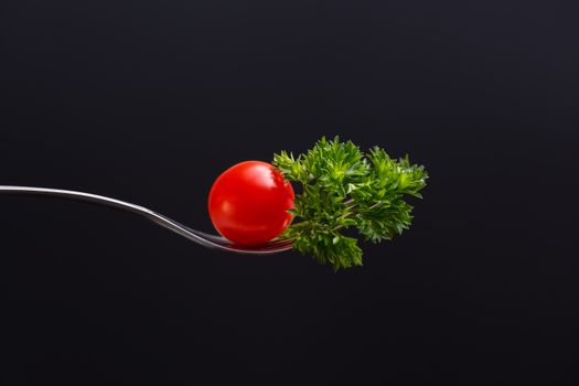 Composition of ripe red cherry tomato and green parsley on fork representing concept of healthy food
