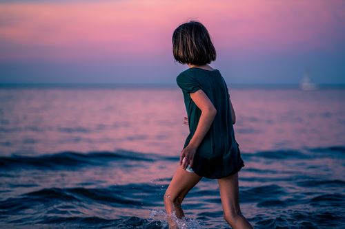 Free Side view of faceless little girl running in wavy water of sea in summer evening Stock Photo