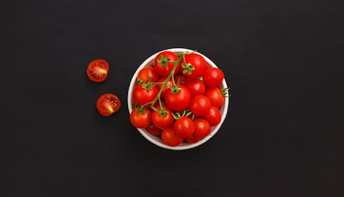 Bowl with ripe cherry tomatoes on black background