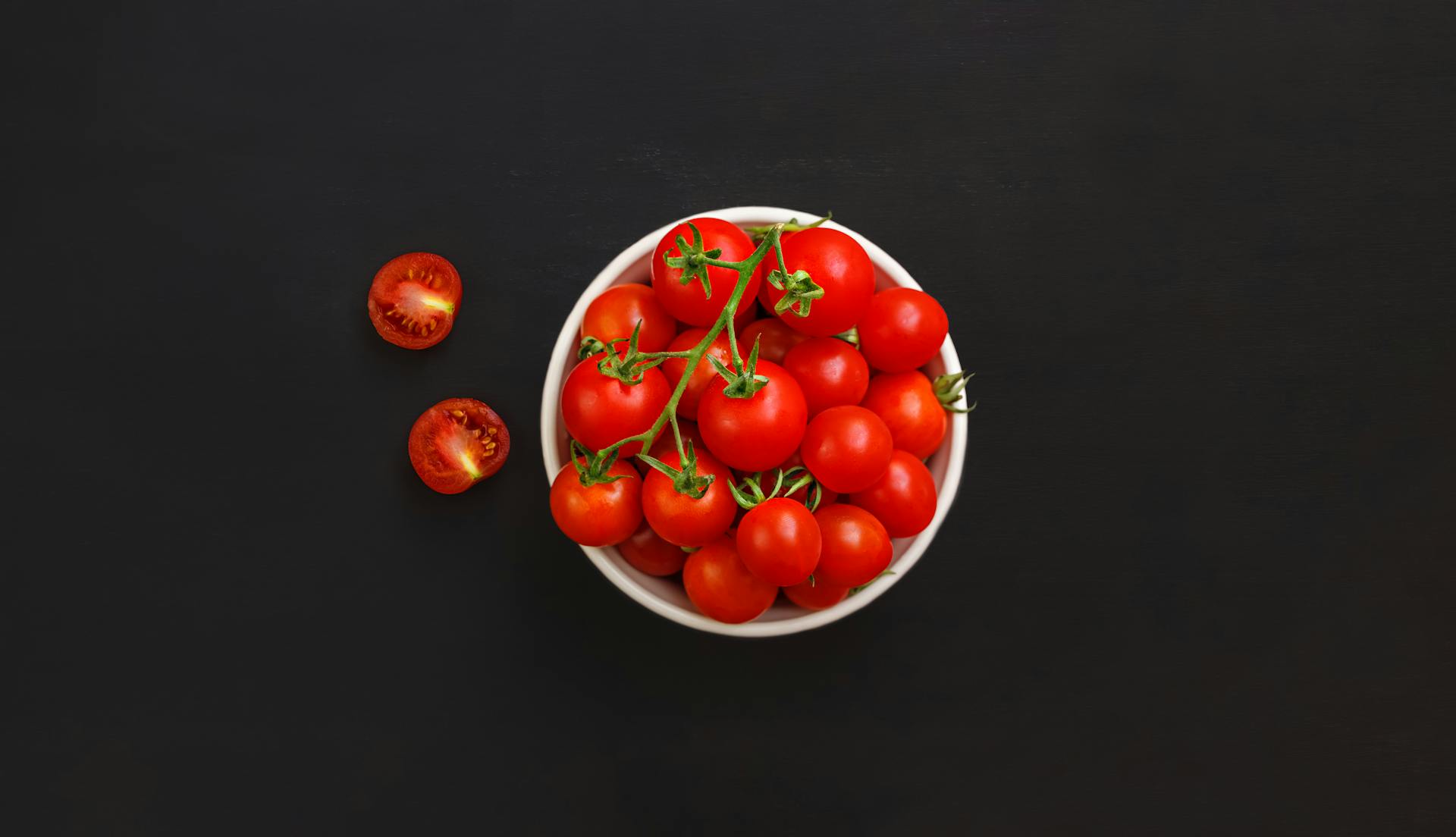 Bowl with ripe cherry tomatoes on black background