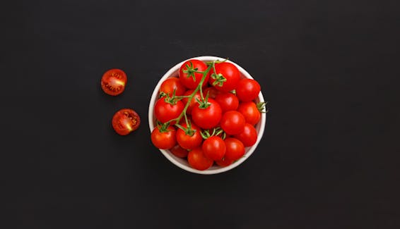 Bowl with ripe cherry tomatoes on black background
