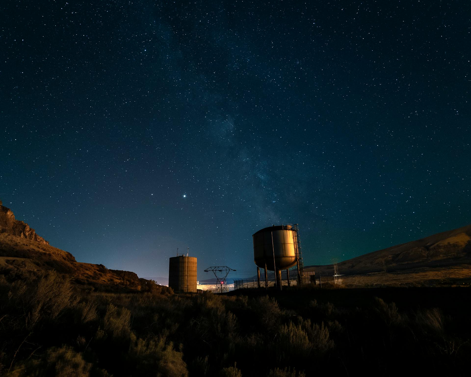 Water towers silhouetted against a starry sky in Rock Island, WA, capturing the Milky Way's splendor.