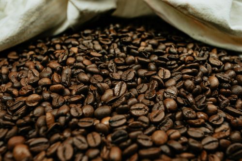 Free From above of pile of spilled cut brown coffee beans with pleasant aroma near textile Stock Photo