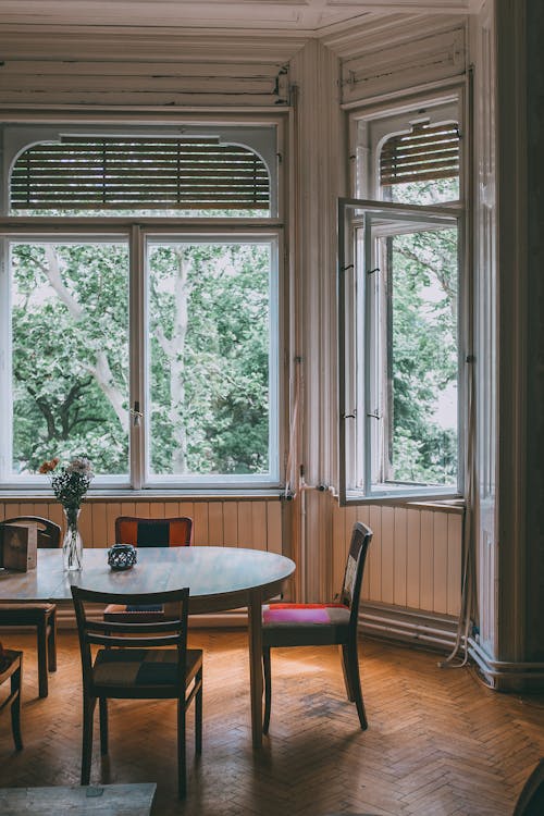 Interior of classic dining room with vintage wooden furniture and big windows overlooking green garden in daylight