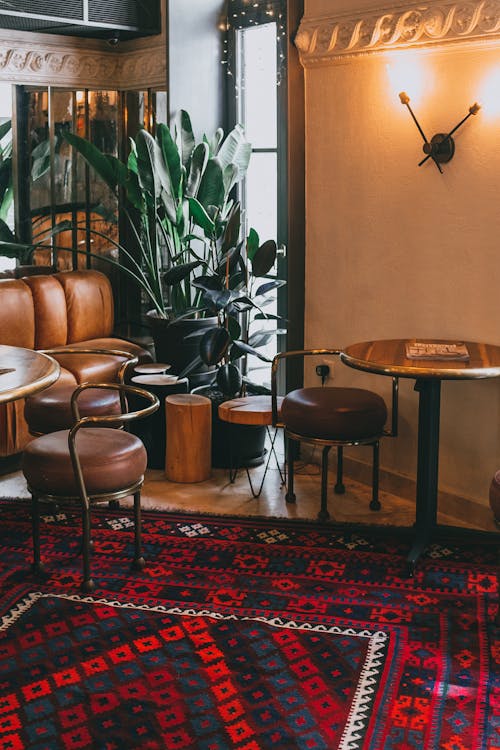 Classic styled wooden tables and leather chairs in cozy cafe with ornamental rug and potted plants