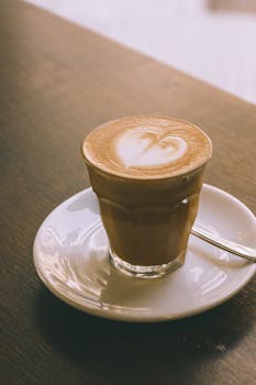A beautifully crafted latte with heart-shaped foam served in a glass, perfect for café ambiance.