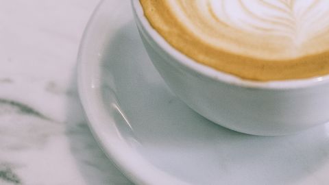 From above cup of appetizing hot foamy cappuccino with latte art placed on marble table in cafe