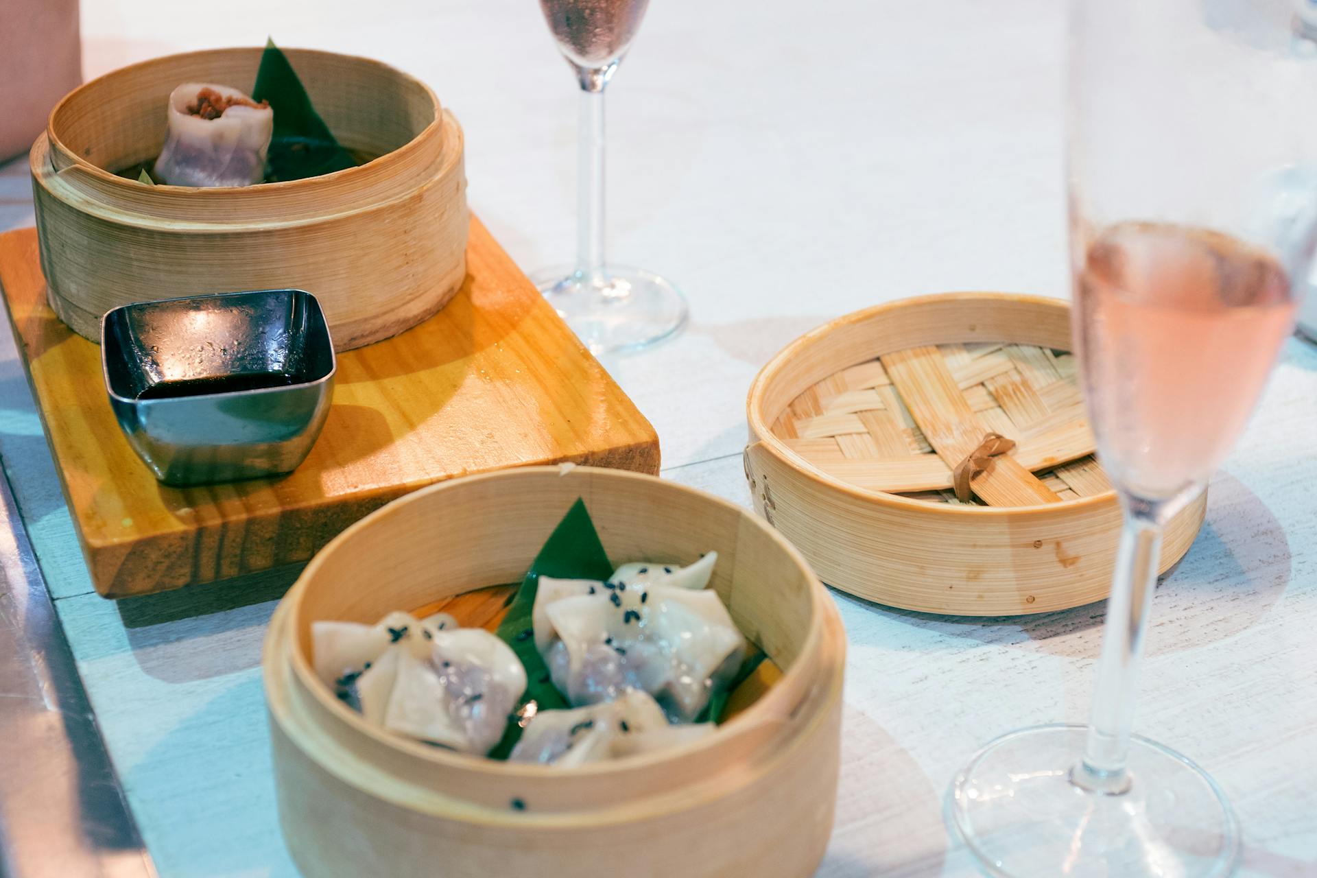 Exquisite dim sum served with champagne in a bamboo steamer set on a wooden board.