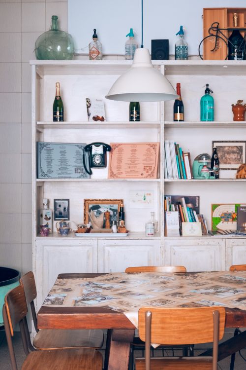 Free Wooden dining table with chairs placed in cozy kitchen near shelves with various decorations and bottles Stock Photo