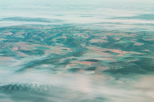 Aerial view of white clouds floating over terrain with various agricultural fields and lush hills in countryside