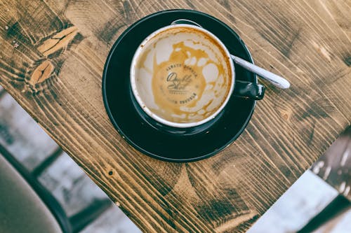 From above of stain of drunk coffee in ceramic cup placed on wooden table with saucer in stylish cafe