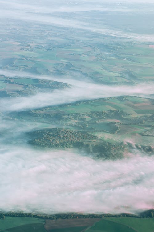 Aerial view of agricultural green terrain covered with grass and thick fog on plantations in summer morning in rural area