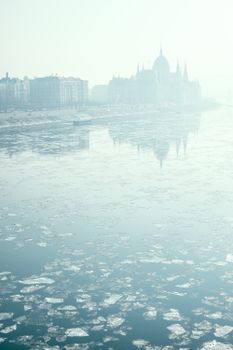 一个多雾的冬日清晨，城市建筑的倒影映在河面的浮冰上