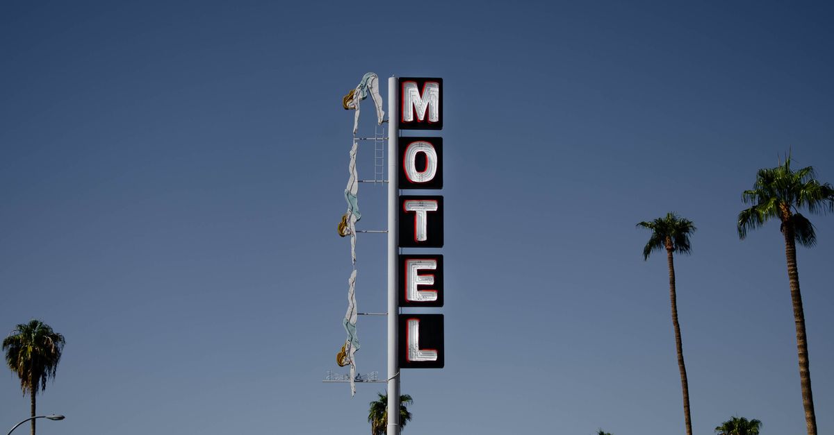 Low angle of motel signboard on metal pillar located at roadside near tall palms against cloudless blue sky