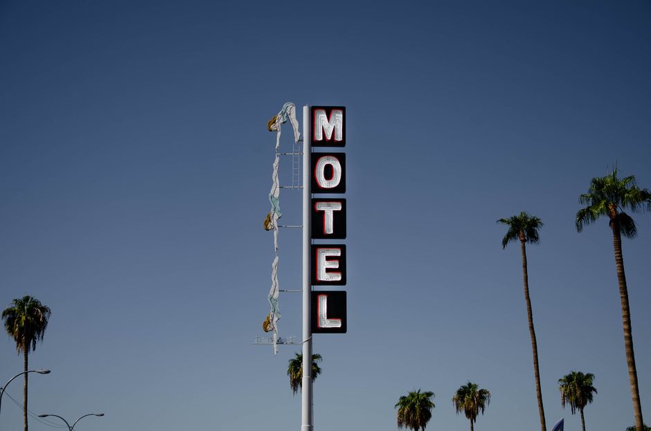 Low angle of motel signboard on metal pillar located at roadside near tall palms against cloudless blue sky