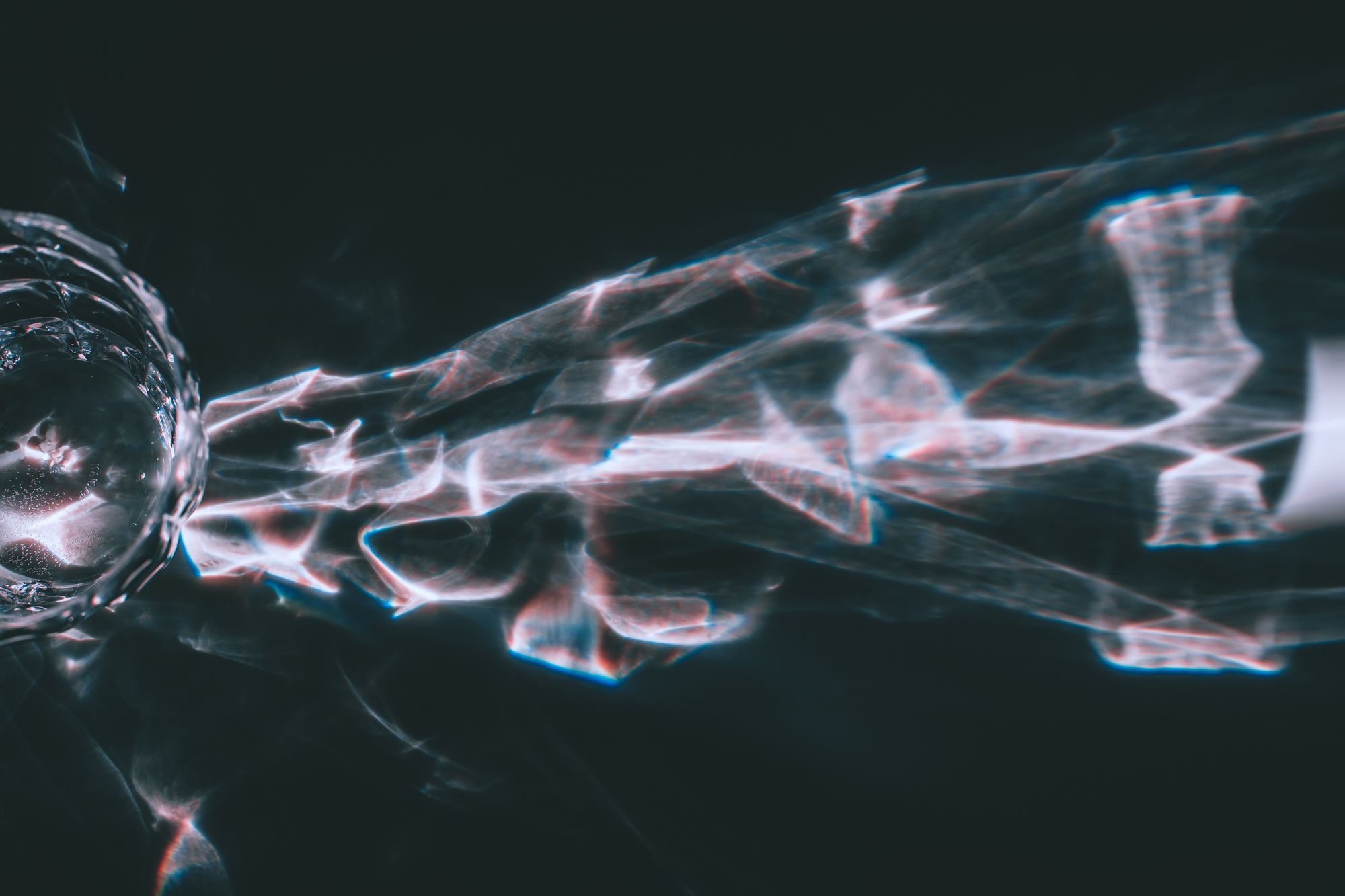 From above bright ray of light shining through faceted glass and reflecting on black background in dark room