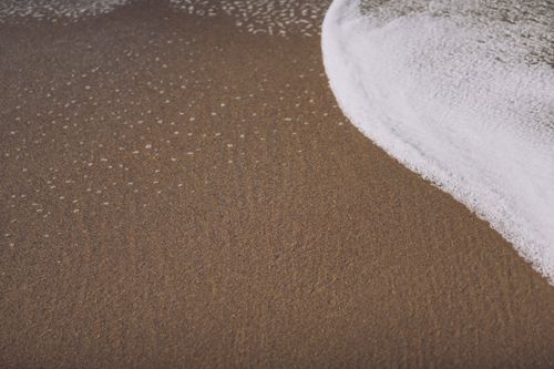 Free From above of sandy coast with ripples and foamy sea water in daytime Stock Photo