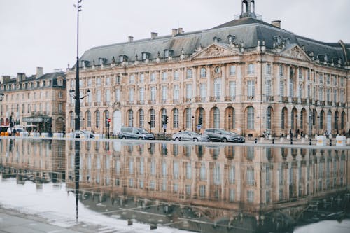 Square with Garonne river and aged house facades near road with cars in Bordeaux