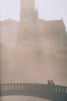 大雾天气中，桥上难以辨认的夫妇旅行者剪影，与旧寺庙和城市建筑相对