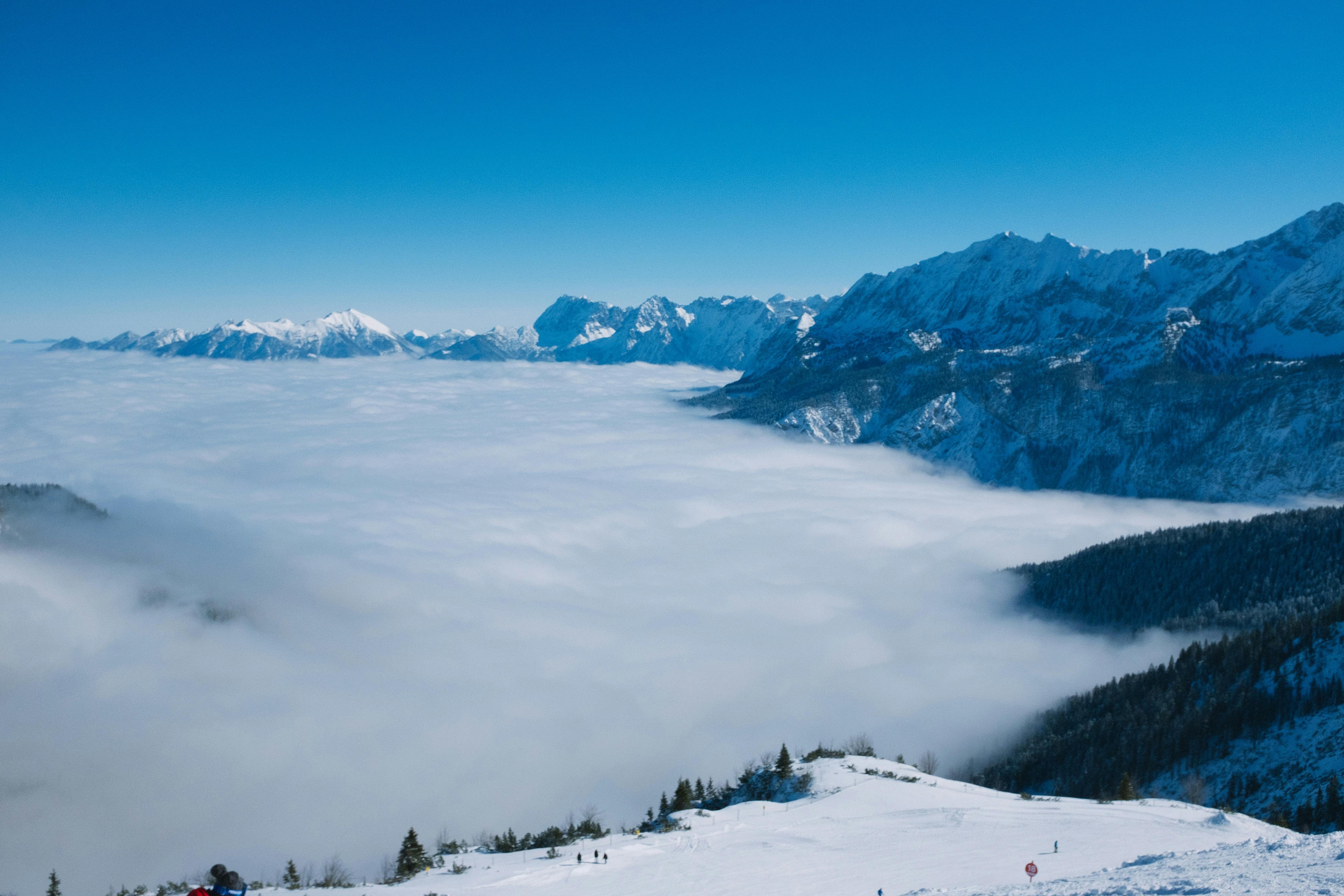 Snowy mountains with trees under blue sky on foggy day